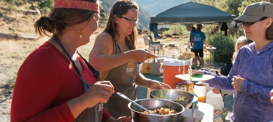multi day rogue river rafting and camping three women serving food at a river campsite on the rogue river