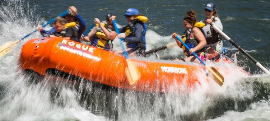 rogue family rafting a group of people in an orange raft while river rafting