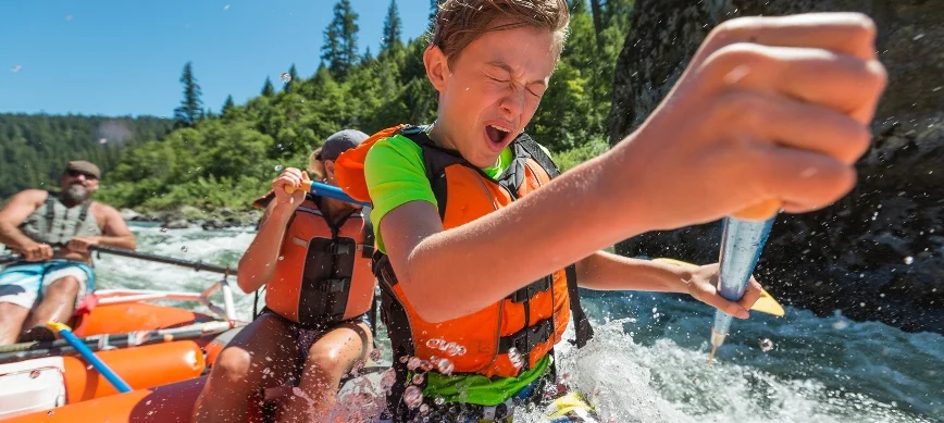 rogue river family rafting a young boy paddles a whitewater raft and gets splashed